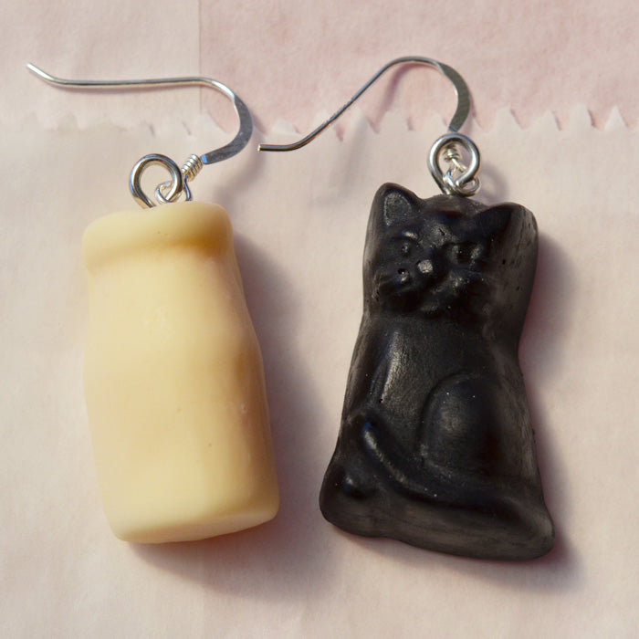 close up of white milk bottle and black cat lolly novelty earrings made from resin on a white background