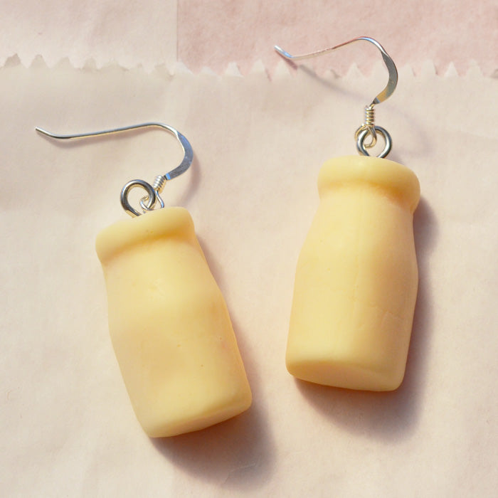 Close up of white milk bottle lolly novelty earrings made from resin on a white lolly bag background