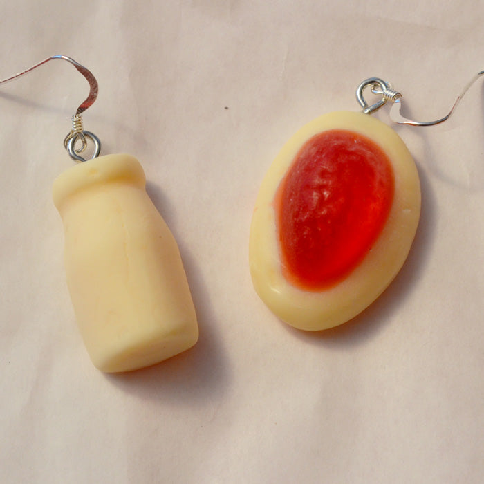 close up of white milk bottle and red and white strawberry and cream lolly novelty earrings made from resin against a white background