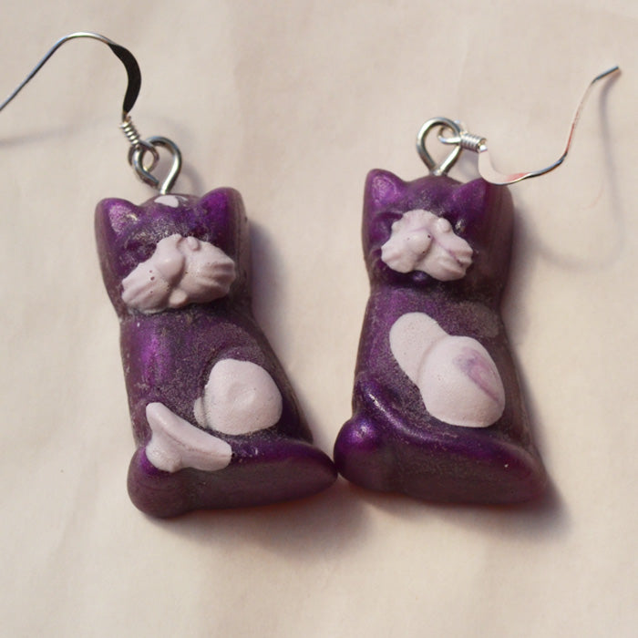 Close up of purple cat lolly novelty earrings made from resin with lilac spots on a white background