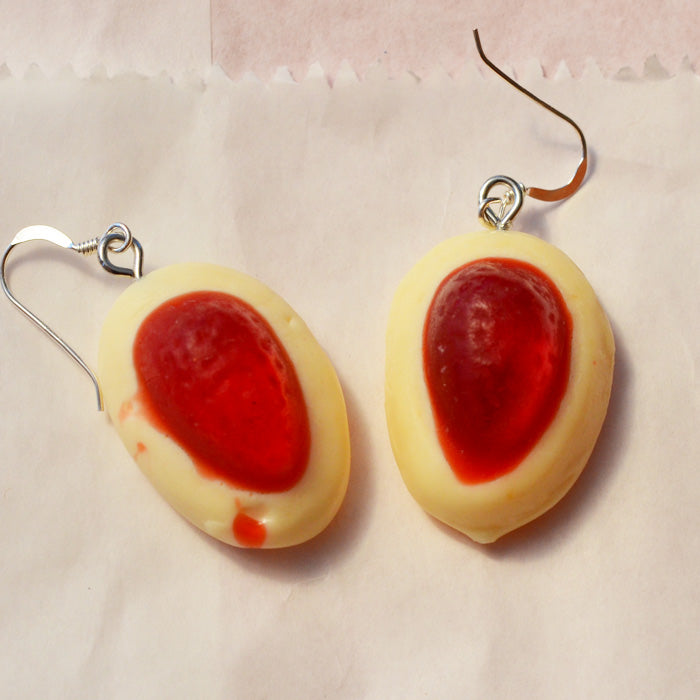 close up of red and white strawberry and cream novelty earrings made from resin on a white lolly bag background