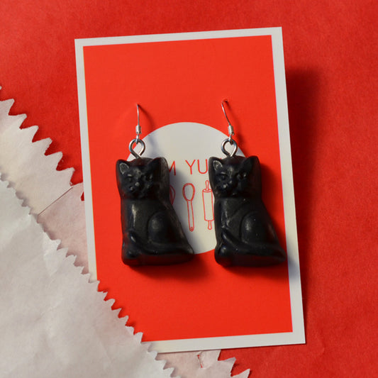 Black Cat Lolly Novelty earrings made from resin on hooks against a white and red background