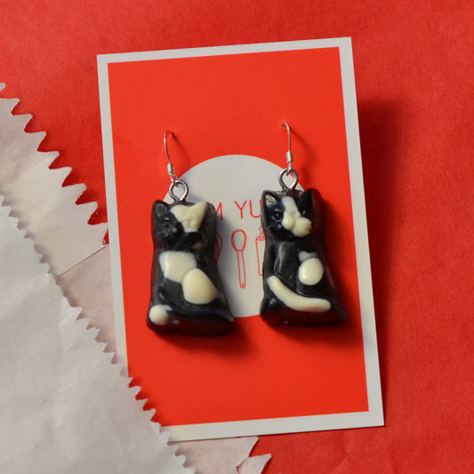 Black lolly cat novelty earrings made from resin with white spot on a white and red background